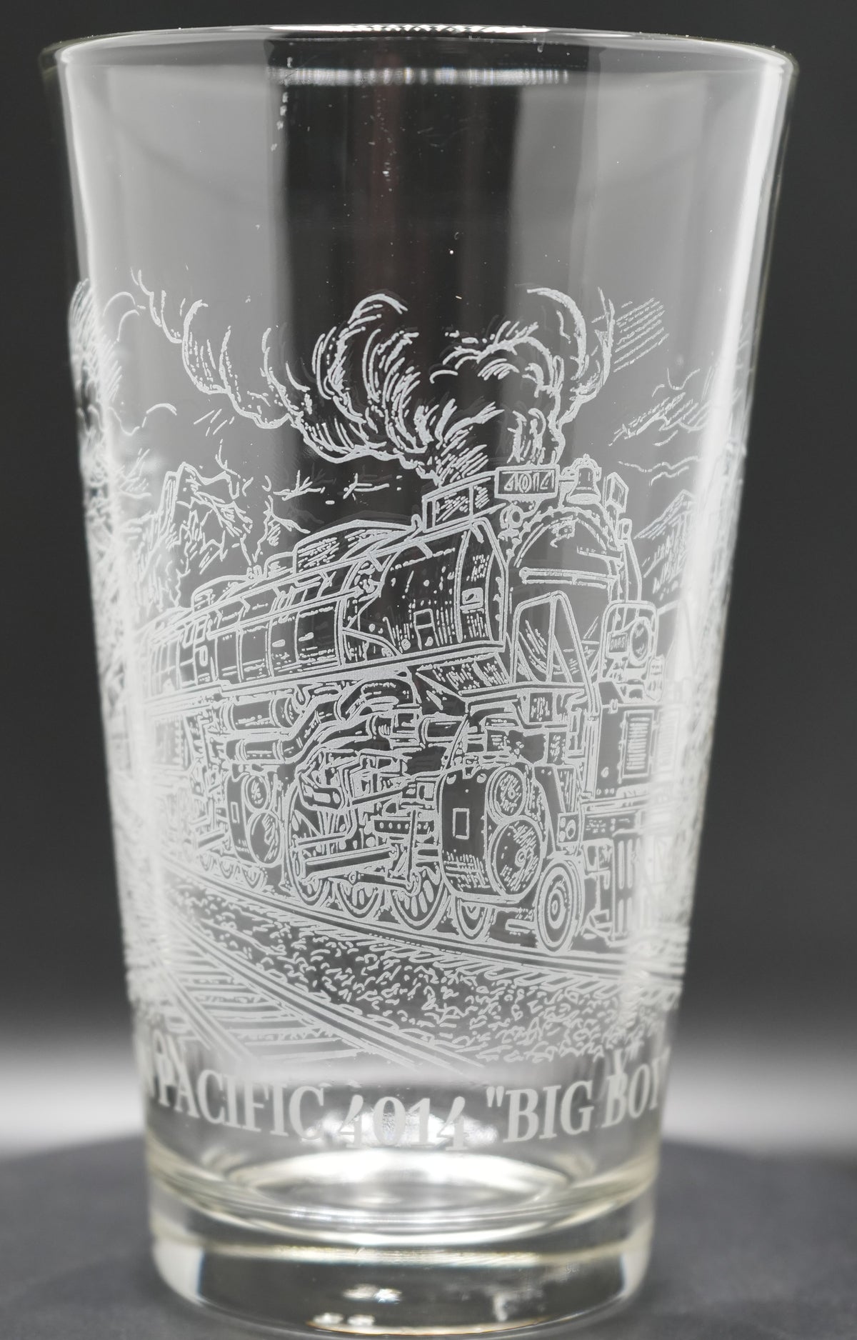 A clear glass pint glass featuring an engraved steam locomotive Union Pacific 4014 "BIG BOY"' on a dark gray background.