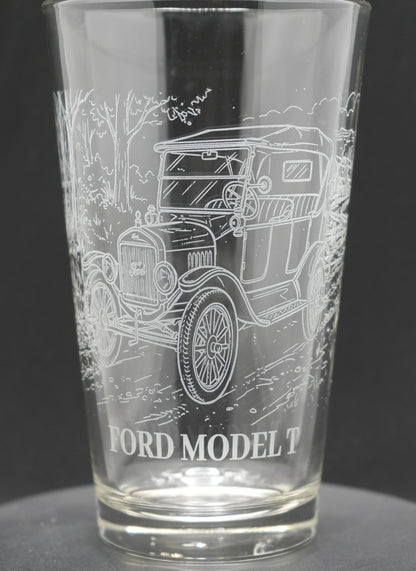 A clear glass pint tumbler featuring an etched white line drawing of a vintage Ford Model T car, with 'FORD MODEL T' text printed near the base, set against a dark gray background.