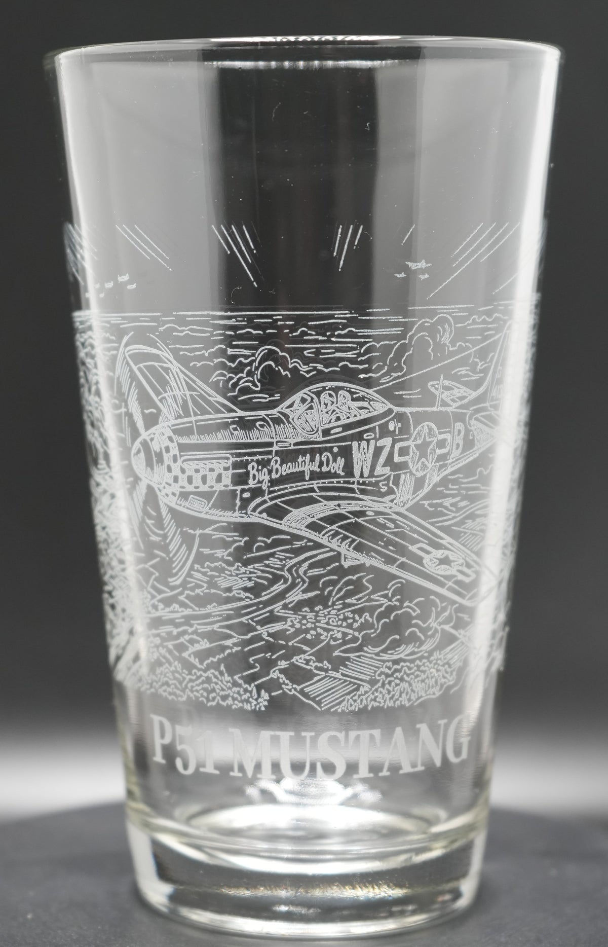 A clear glass pint glass featuring an engraved P-51 Mustang airplane 