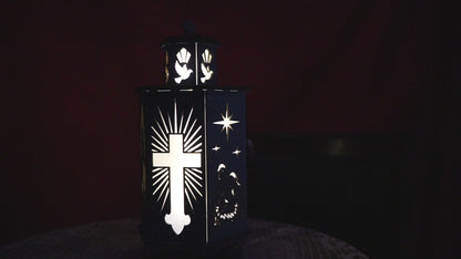 Video showing a blue wooden Christian lantern glowing in the dark, casting warm light through a laser-cut cross, dove, and Nativity scene.